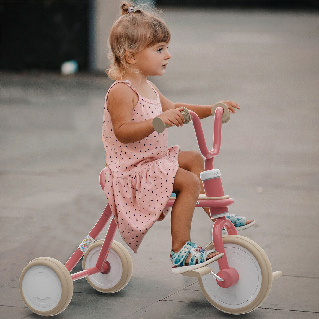 Een peuter in een roze jurk rijdt buiten op een roze Yvolution driewieler.