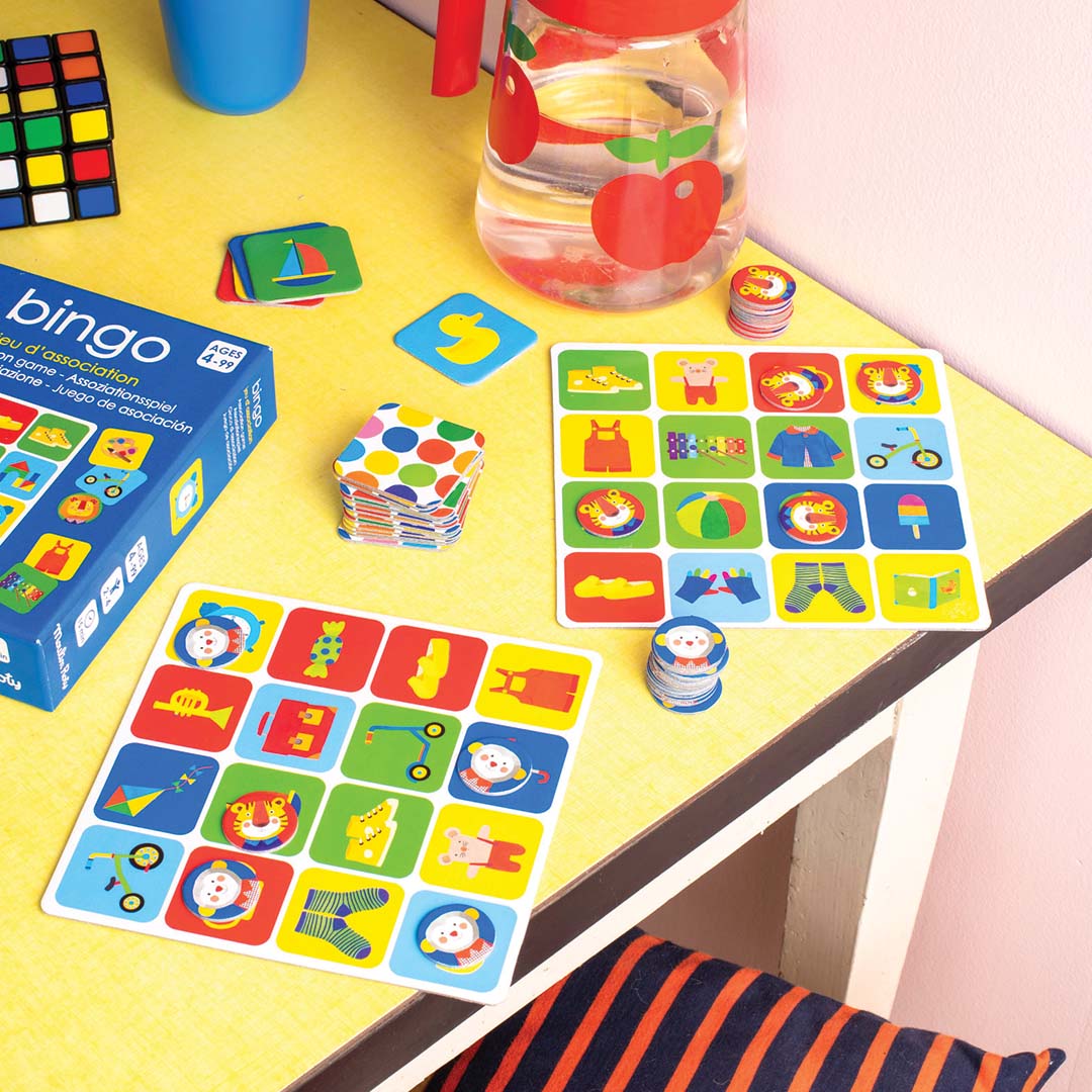 Het Moulin Roty bingo spel uitgestald op een gele tafel met speelkaarten, fiches en de speldoos.