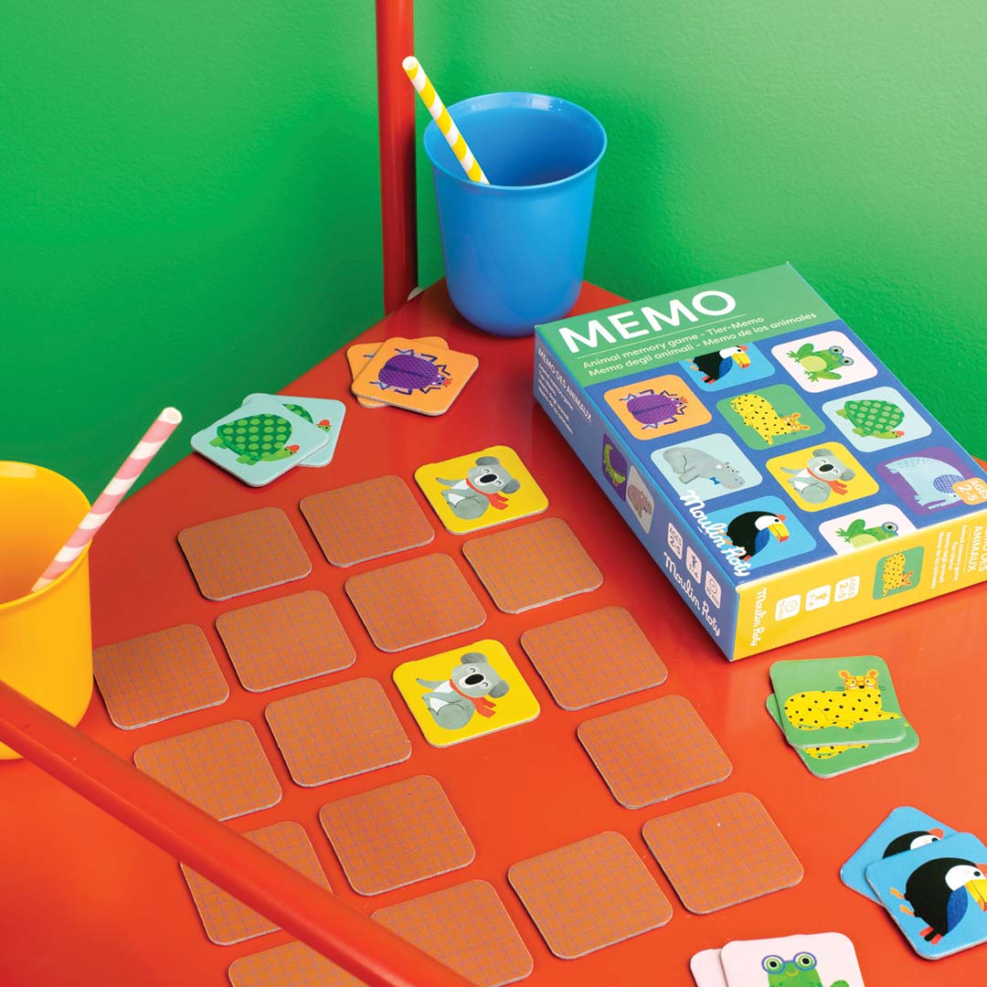 Moulin Roty memorie spel met dierenafbeeldingen, uitgespreid op een rode tafel tijdens het spelen.