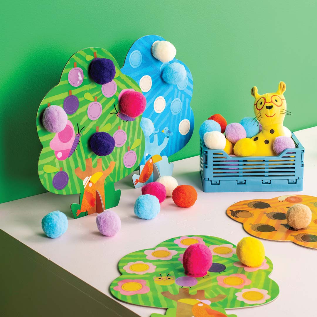 Twee kartonnen bomen van de pompom knutselset gedecoreerd met gekleurde pompoms op een tafel.