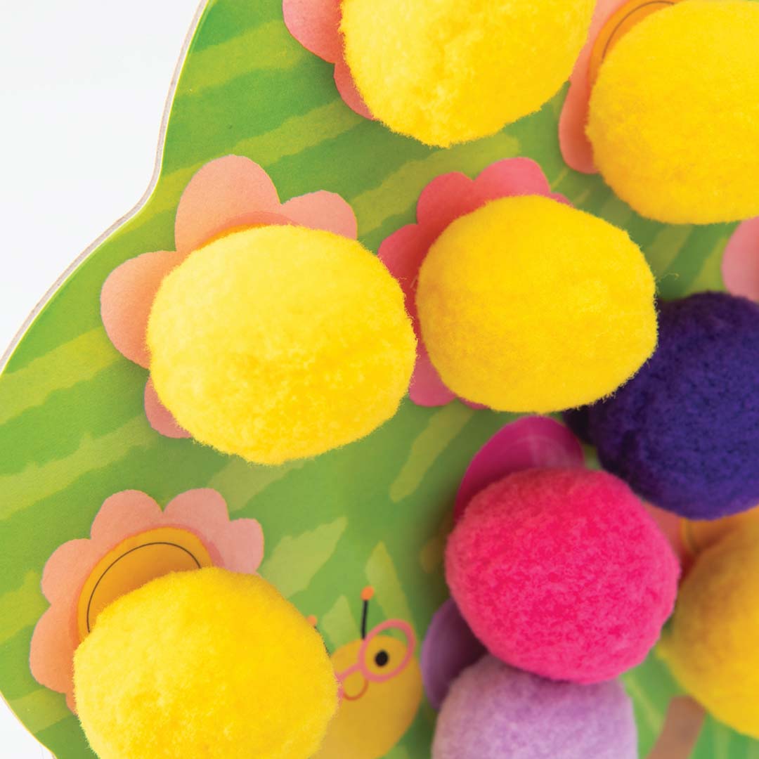 Detail van een groene kartonnen boom met gele, roze en paarse pompoms.