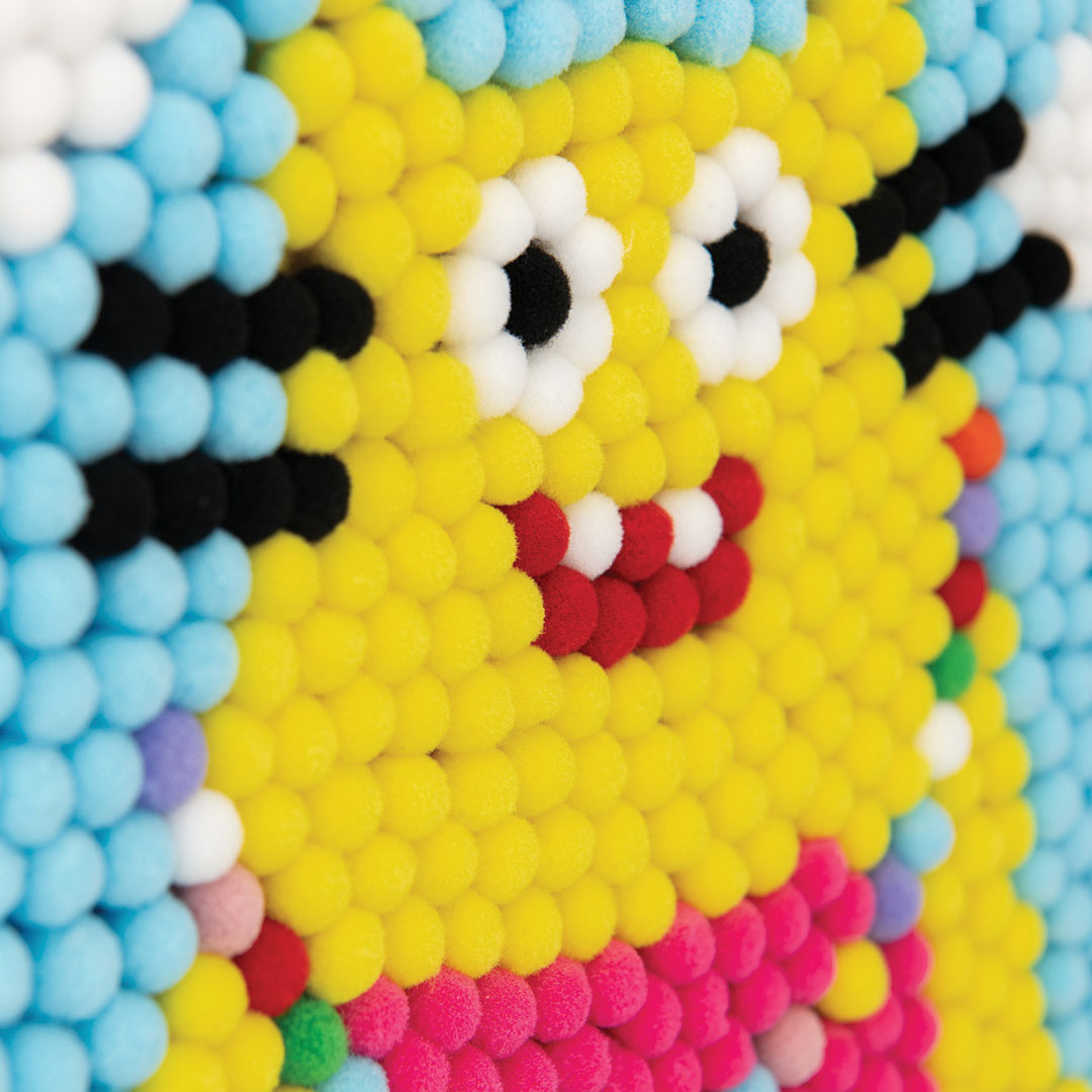 Detail van het gele monstergezicht gemaakt van gele, witte, zwarte en rode pompoms.
