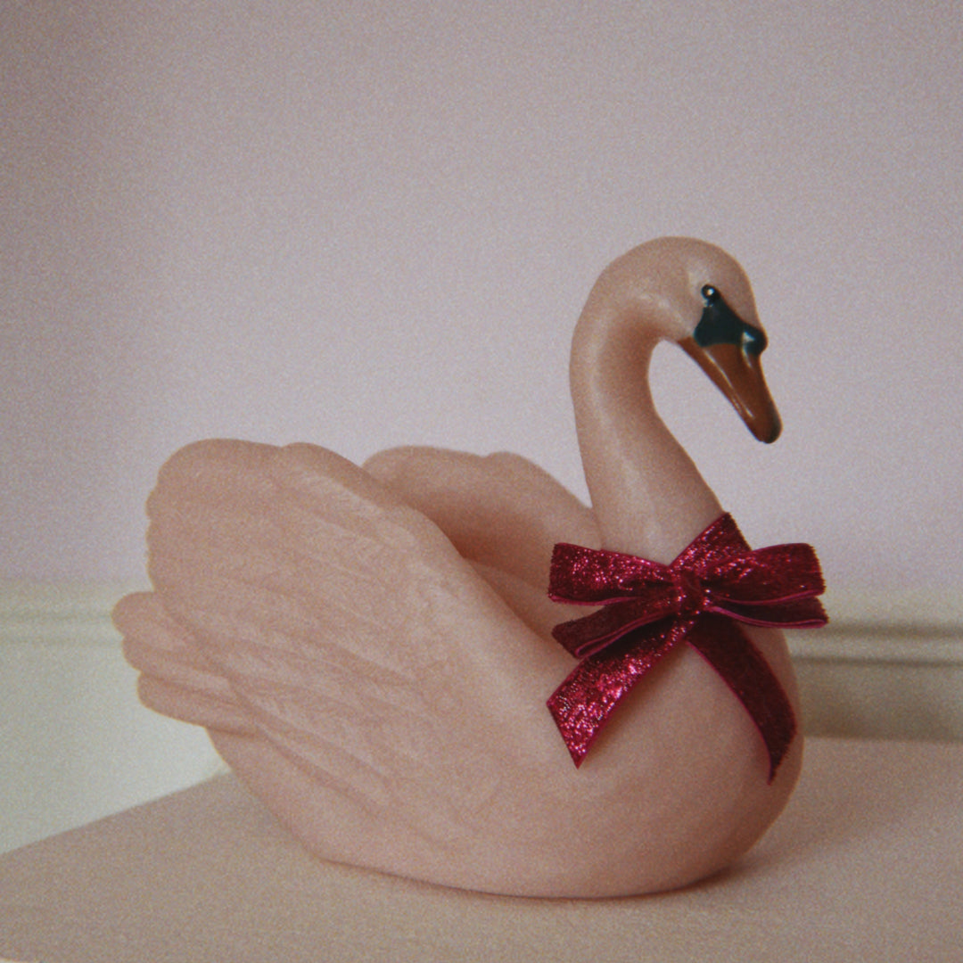 Konges Sløjd roze zwaan LED lamp met een donkerroze glitterstrik, staand op een oppervlak.
