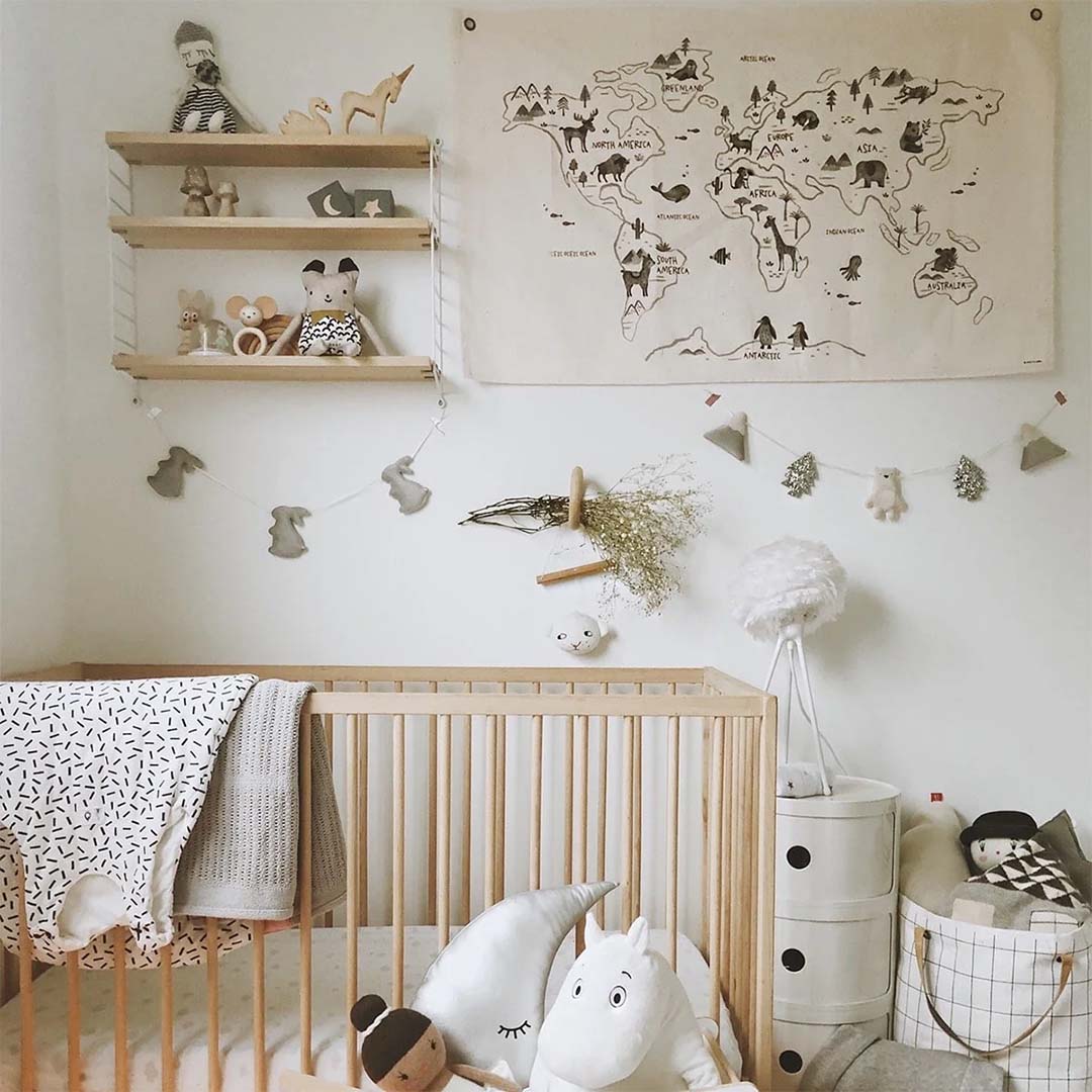 Het rose in April wandkleed met wereldkaart en dieren hangt boven een ledikant in een babykamer.